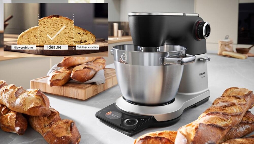 Na obrazie znajduje się robot kuchenny z metalową misą, obok którego leżą bagietki. W lewym górnym rogu widoczny jest przekrój chleba z tekstem: \'Niewyrobione\', \'Idealne\', \'Zbyt długo wyrabiane\'.