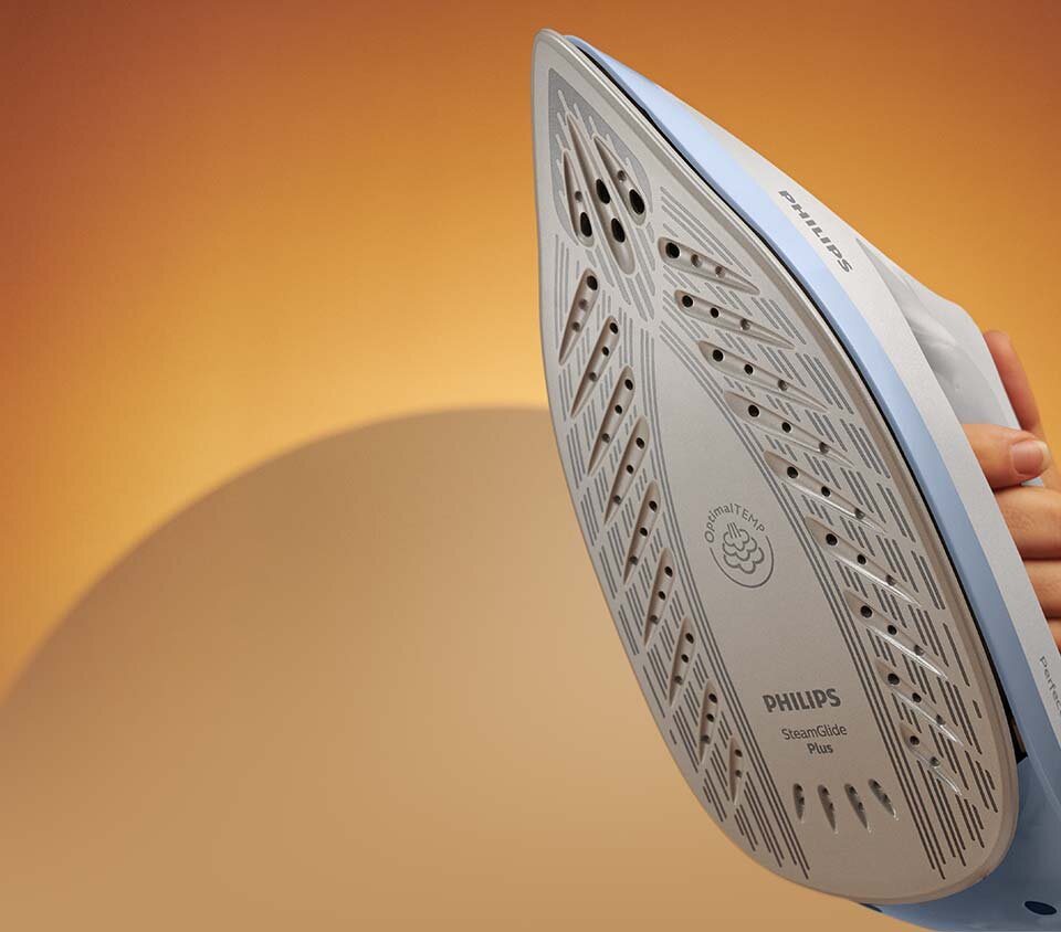 Zdjęcie przedstawia stopę żelazka z widocznymi otworami parowymi i napisami: \'OptimalTEMP\', \'PHILIPS\', \'SteamGlide Plus\'. W tle znajduje się jednolite, pomarańczowe tło.