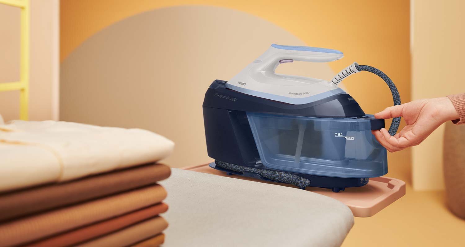 Na obrazie widoczny jest generator pary z przezroczystym zbiornikiem na wodę, trzymany przez osobę. Na urządzeniu znajduje się logo \'PHILIPS\' oraz napis \'1.8L MAX\'.