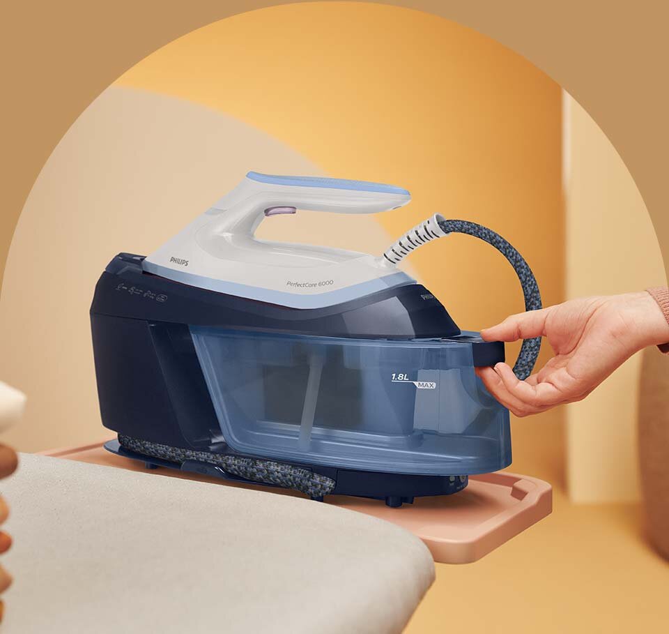 Na obrazie widoczny jest generator pary z napisem \'PHILIPS PerfectCare 6000\' oraz \'1.8L MAX\'. Osoba trzyma ręką uchwyt urządzenia.