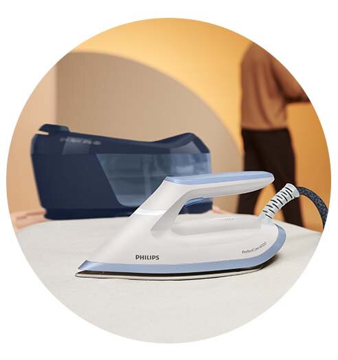 Na obrazie widoczny jest generator pary marki PHILIPS z napisem \'PerfectCare 6000\'. W tle znajduje się osoba oraz część urządzenia z przezroczystym zbiornikiem na wodę.
