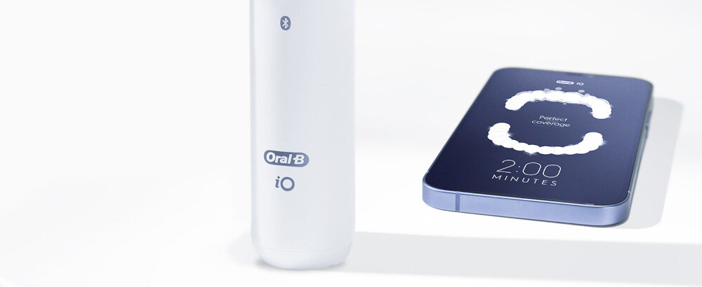 Na obrazie widoczna jest biała szczoteczka z logo \'Oral-B iO\' oraz smartfon z wyświetlaczem pokazującym grafikę z napisem \'Perfect Coverage\' i \'2:00 MINUTES\'.