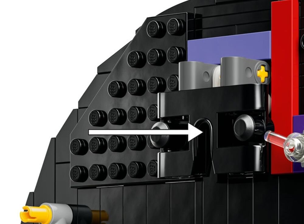 Zbliżenie na czarną konstrukcję z klocków LEGO z widocznymi elementami w kolorze czerwonym, fioletowym i żółtym. Na środku znajduje się biała strzałka wskazująca kierunek.