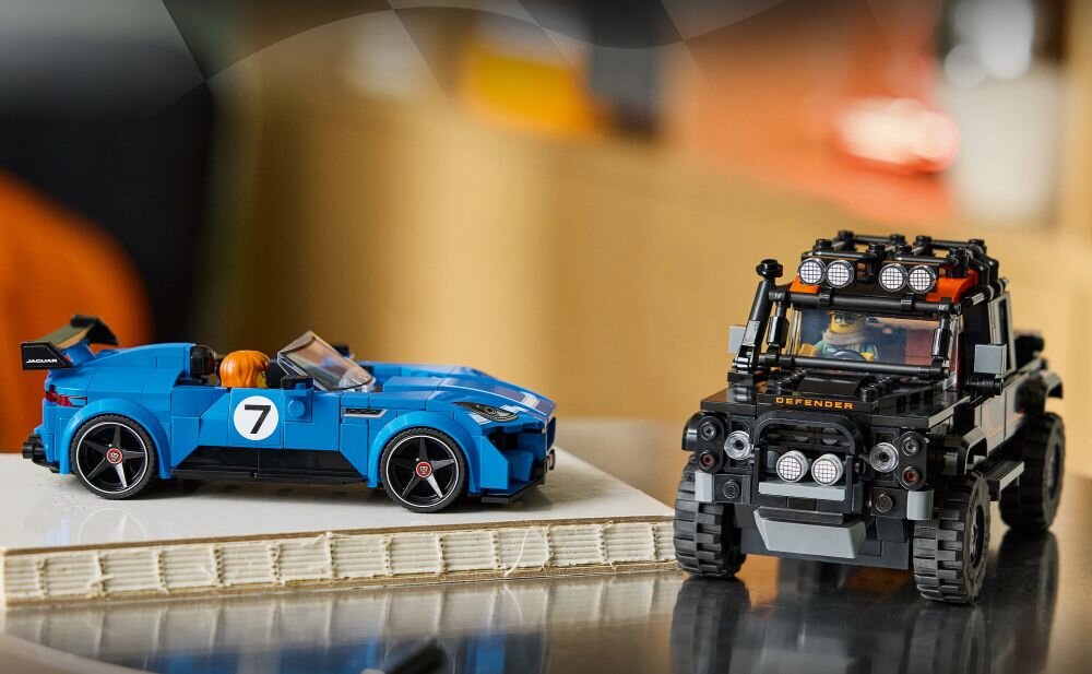 Na obrazie znajdują się dwa modele samochodów z klocków LEGO: niebieski sportowy samochód z numerem 7 oraz czarny terenowy pojazd z napisem \'DEFENDER\' na przodzie. Oba modele są ustawione na jasnej powierzchni, a w tle widać rozmyte elementy wnętrza.