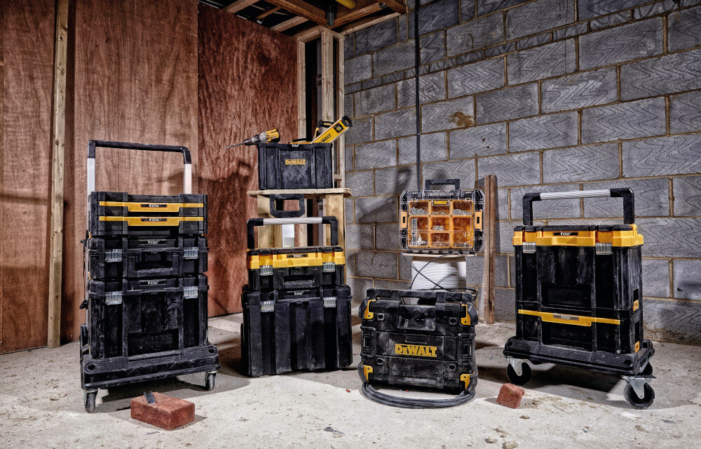 Skrzynka narzędziowa DEWALT DWST1-71228 magazyn pomieszczenie drewniana ściana betonowa ściana kilka skrzynek ustawionych na podłodze jedna na drugiej specjalne zaczepy łączenie skrzyni z innymi elementami systemu T-STAK modułowa konstrukcja ułatwia transport narzędzi prządek