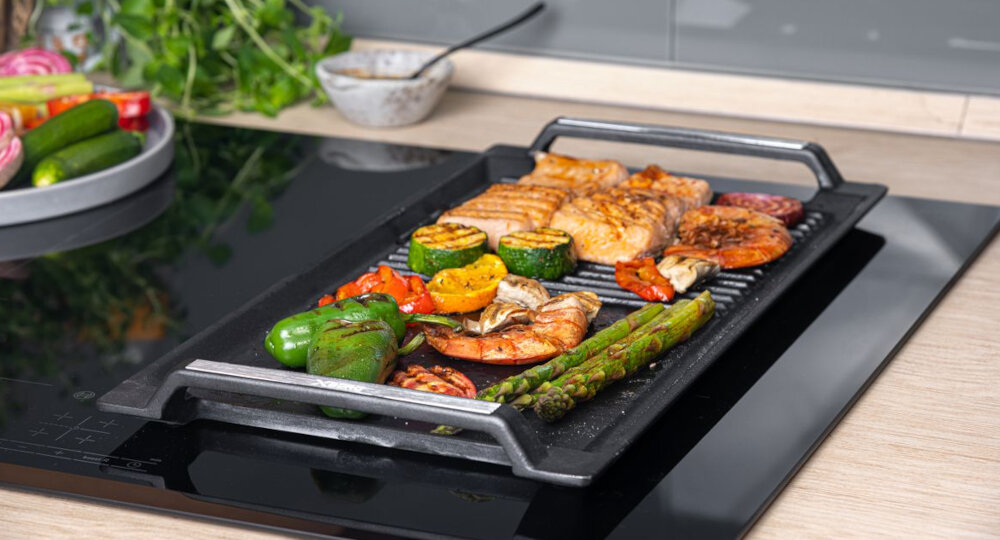 GRILL ŻELIWNY BERG ROSTI Płyta grillowa z grillowanymi warzywami i rybą umieszczona na płycie indukcyjnej