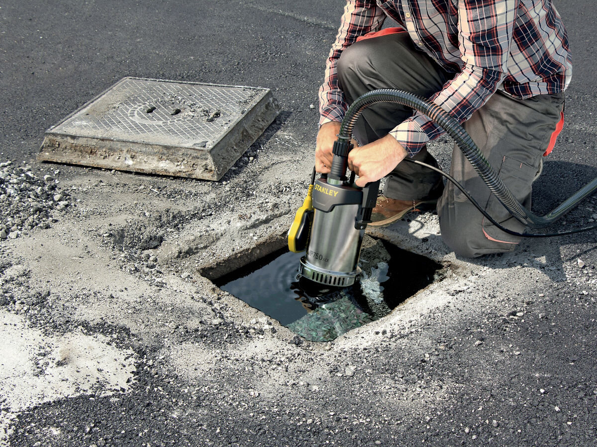 Pompa do wody STANLEY SXUP750XCE elektryczna, woda, odpompowanie, budowa, zalanie, osoba obsługuje pompe do wody w wyciętym asfalcie