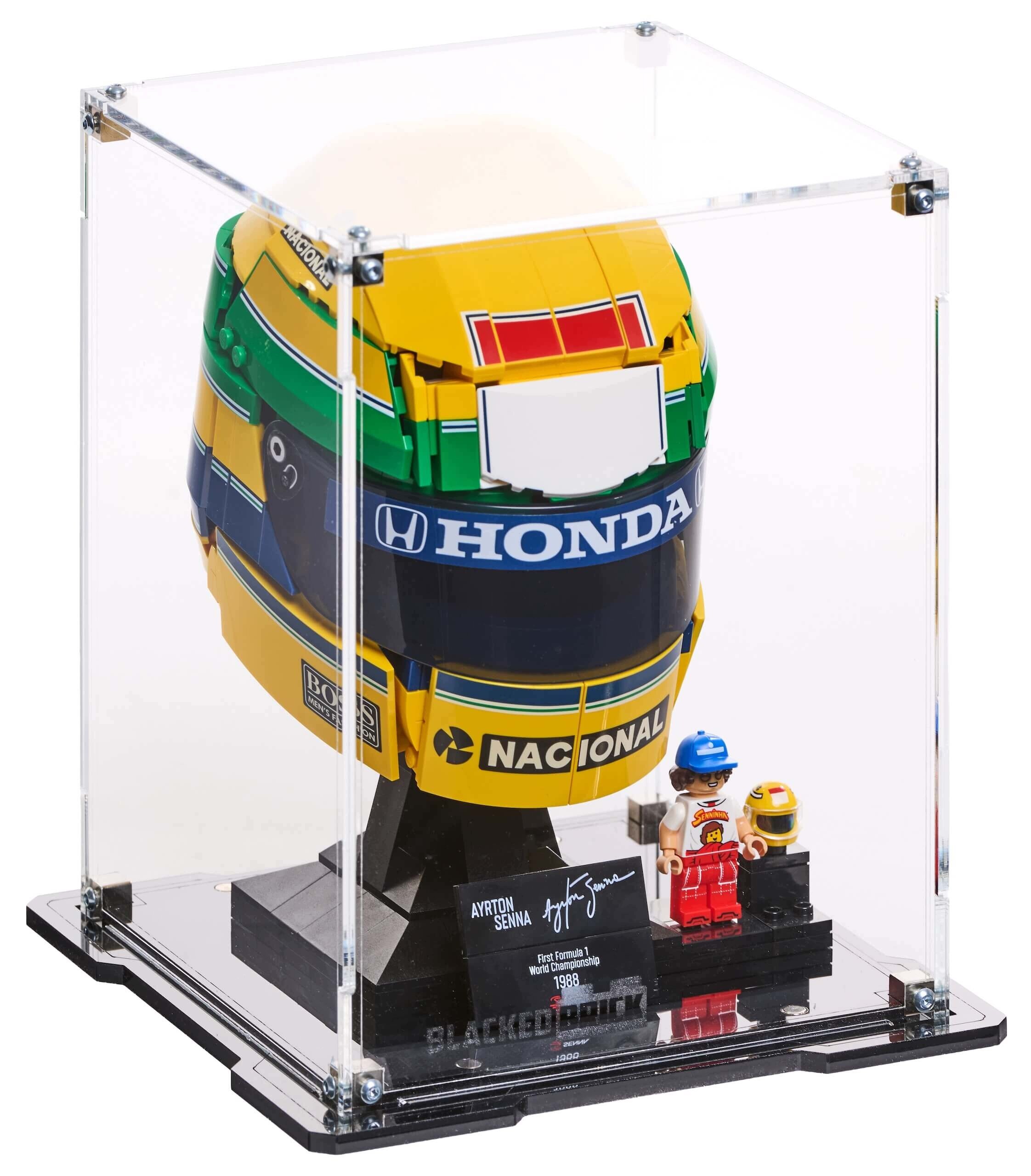 Gablota prezentuje model kasku z klocków LEGO z napisami \'HONDA\' i \'NACIONAL\'. Obok znajduje się figurka LEGO oraz tabliczka z napisem \'AYRTON SENNA\' i podpisem.