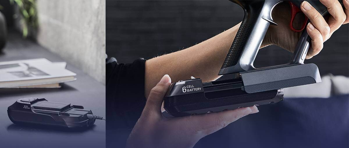 Osoba trzyma odkurzacz pionowy z widoczną baterią oznaczoną jako \'6 CELL BATTERY\'. Obok leży ładowarka z napisem \'72W\'.