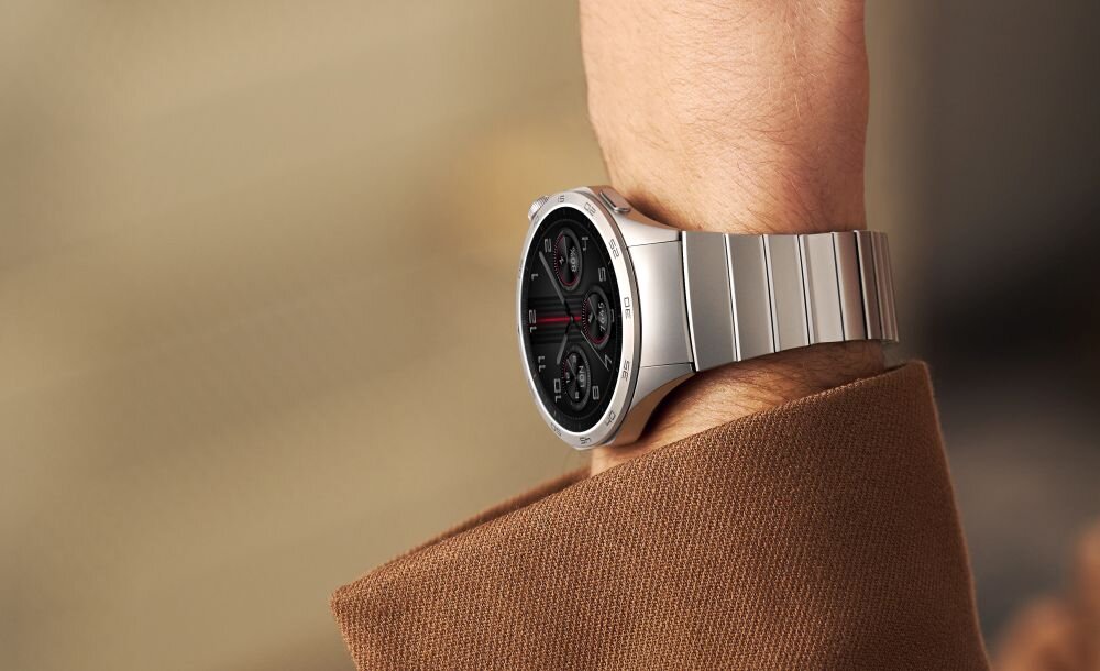 Osoba nosi smartwatch z metalową bransoletą i okrągłą tarczą z trzema małymi cyferblatami. Zegarek ma elegancki, nowoczesny design.