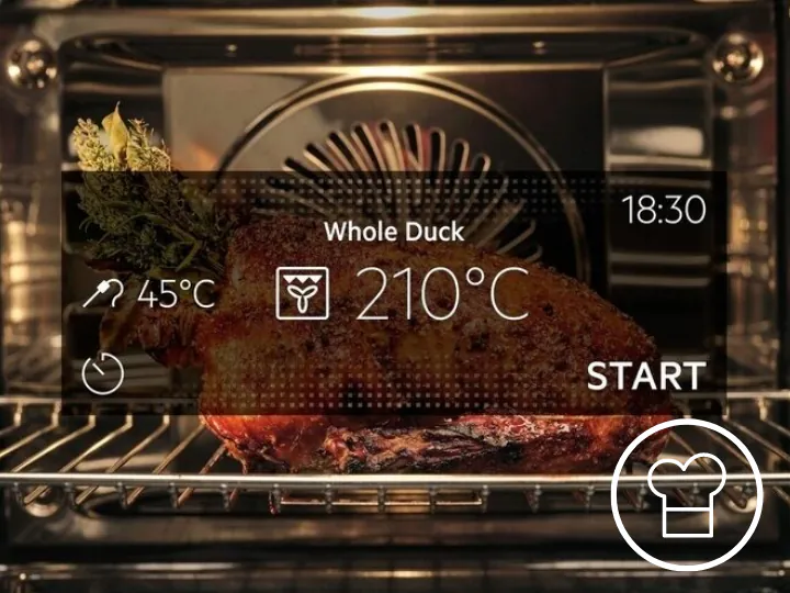 W piekarniku znajduje się pieczona kaczka z ziołami, a na ekranie wyświetlają się informacje: \'Whole Duck\', \'45°C\', \'210°C\', \'18:30\', \'START\'.