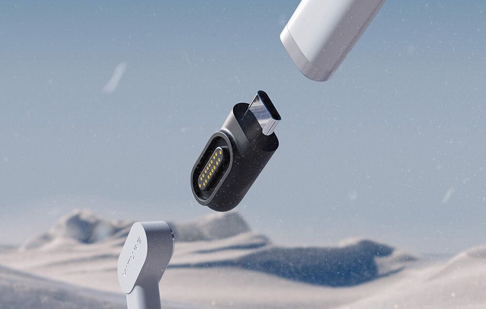 Obraz przedstawia złącze magnetyczne USB-C w kolorze czarnym, unoszące się w powietrzu na tle zimowego krajobrazu. Widoczne są również dwa inne elementy w kolorze białym i szarym, z jednym z nich oznaczonym napisem \'Viture\'.