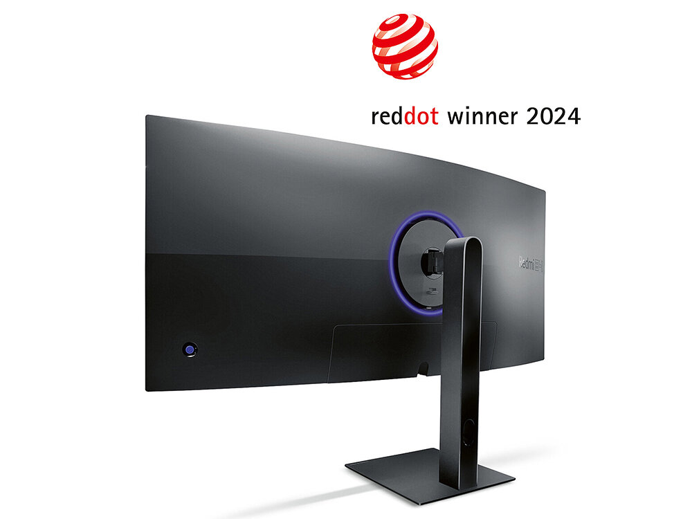 Monitor o zakrzywionym ekranie z widocznym logo \'reddot winner 2024\' nad nim. Monitor jest zamontowany na prostokątnej podstawie, a z tyłu widoczny jest okrągły element dekoracyjny.