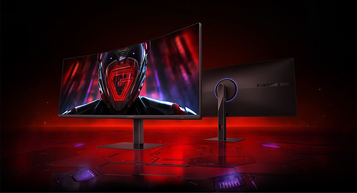 Na obrazie widoczny jest zakrzywiony monitor z wyświetlonym na ekranie futurystycznym hełmem. W tle widać drugi monitor z logo XIAOMI na obudowie.
