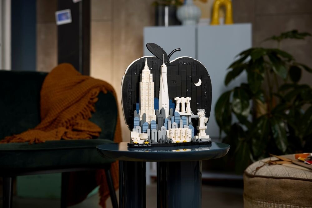 Model LEGO przedstawiający panoramę Nowego Jorku w kształcie jabłka, ustawiony na stoliku w pomieszczeniu. W tle widoczne są meble i rośliny.