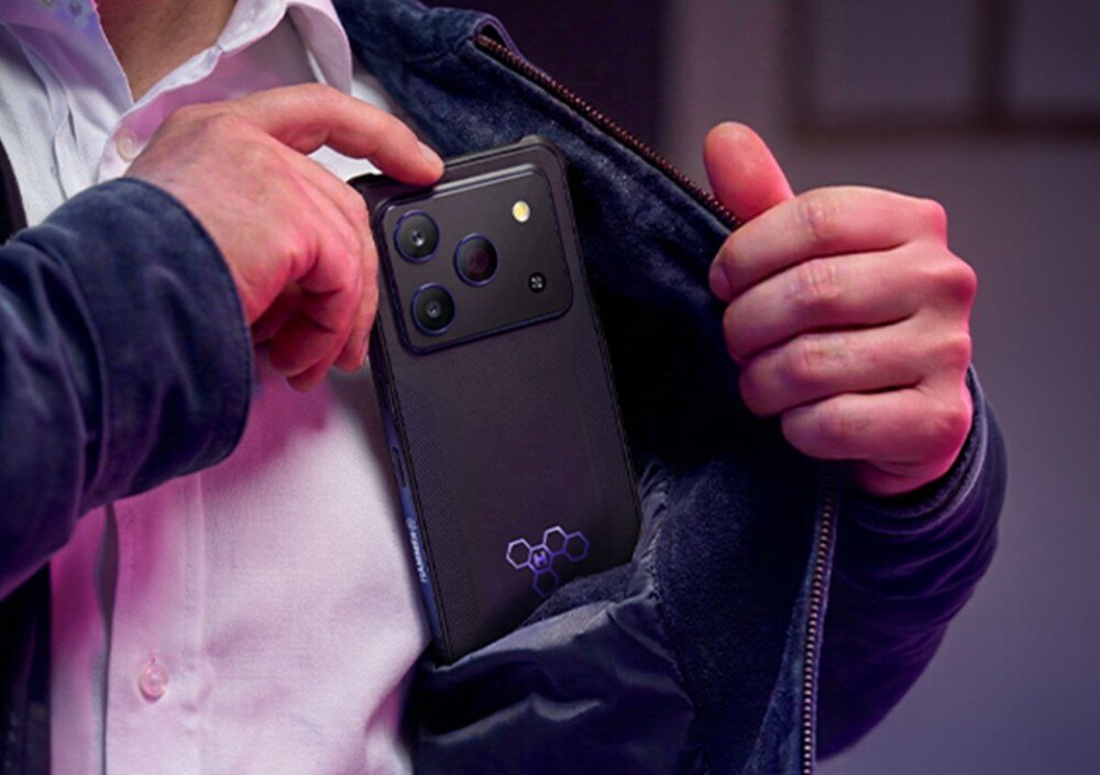Smartfon HAMMER Blade 6 Pro 5G Mężczyzna wkładający pancerny smartfon do wewnętrznej kieszeni kurtki, widoczna tylna obudowa urządzenia z aparatami i świecącym logo