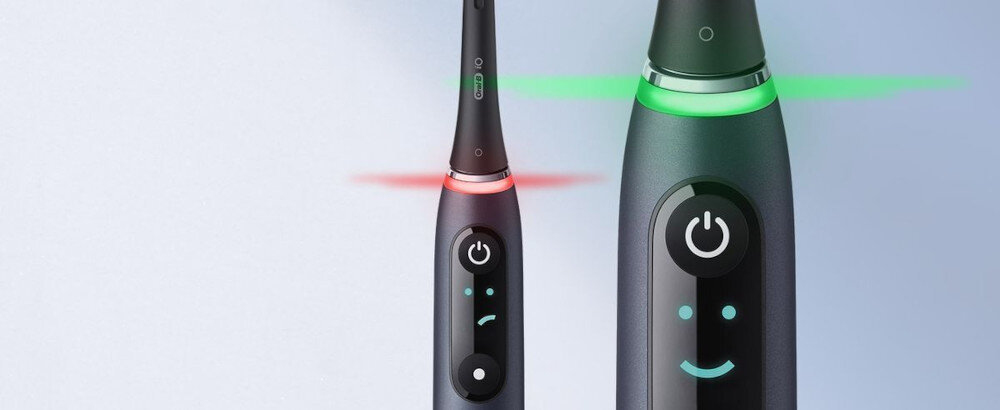 Dwie elektryczne szczoteczki do zębów z wyświetlaczami LED, jedna z czerwonym, a druga z zielonym podświetleniem. Na wyświetlaczach widoczne są ikony twarzy i przyciski zasilania.