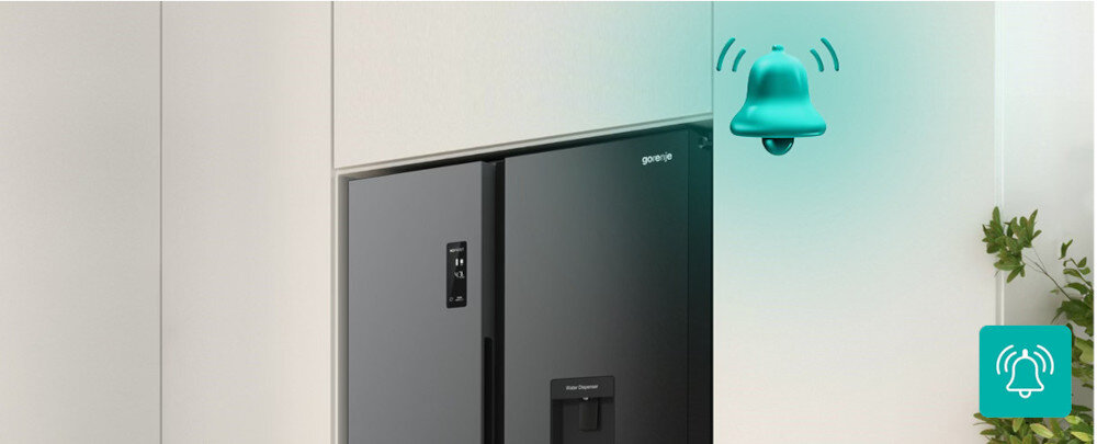 Czarna lodówka z podajnikiem wody i logo \'gorenje\' na drzwiach. Obok lodówki widoczna jest zielona ikona dzwonka z falami dźwiękowymi.