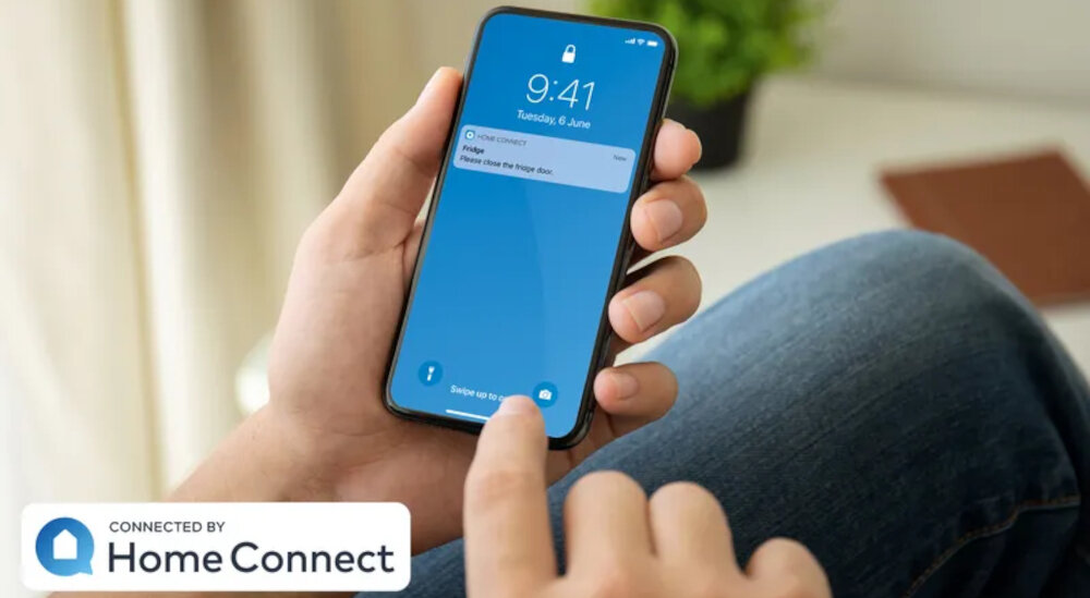 Osoba trzyma smartfon z wyświetlonym ekranem blokady, na którym widnieje godzina 9:41 i data Tuesday, 6 June oraz powiadomienie \'Home Connect: Open Close the Fridge Door\'. W lewym dolnym rogu znajduje się logo i napis \'CONNECTED BY Home Connect\'.