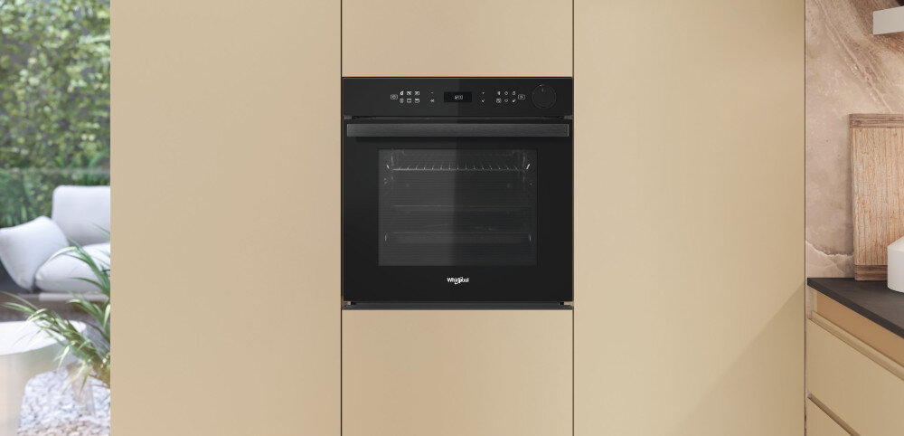 Czarny piekarnik wbudowany w jasną zabudowę kuchenną. Na froncie widoczne jest logo \'whirlpool\'.