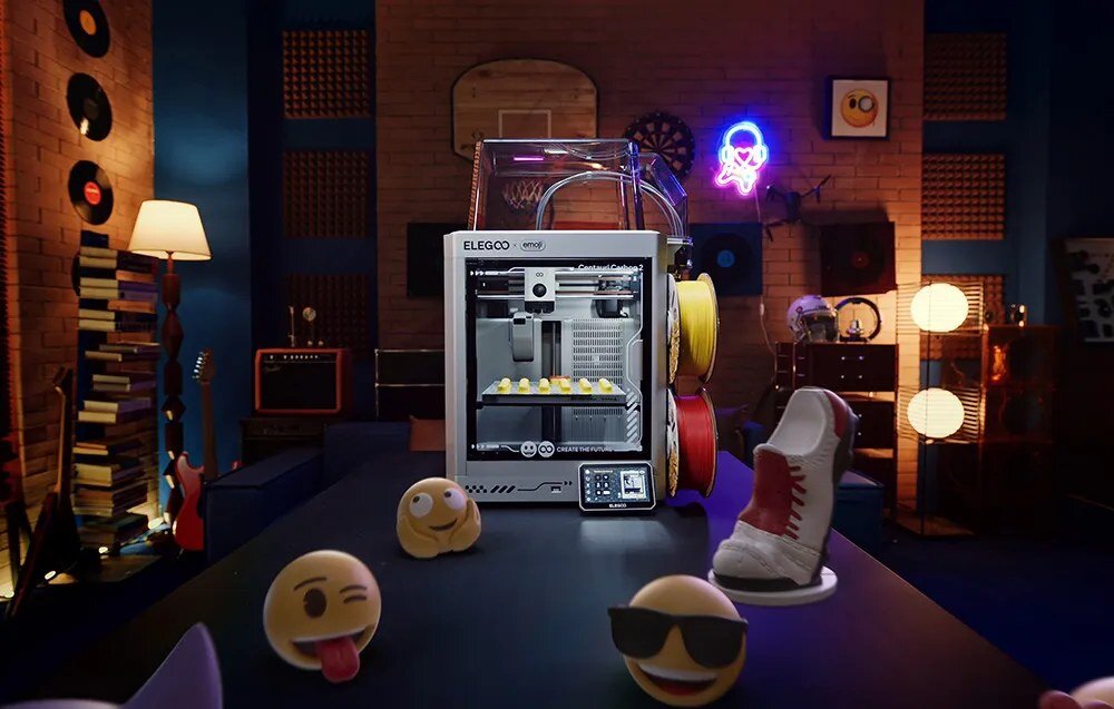 Drukarka 3D ELEGOO x emoji Centauri Carbon 2 Combo obok wydrukowanych figurek emoji.