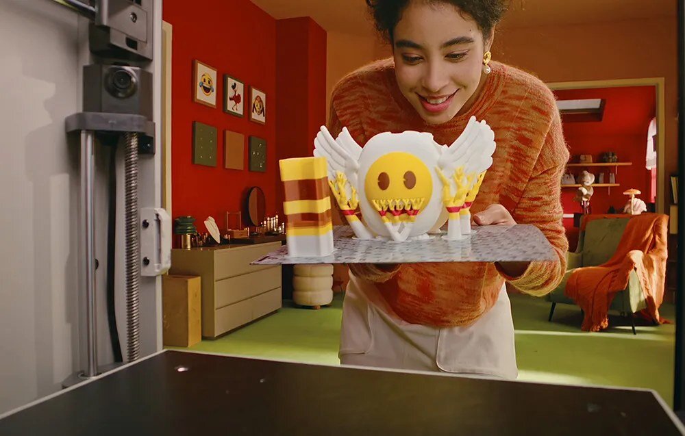 Kobieta przenosząca gotowy druk 3D figurki emoji obok ELEGOO x emoji Centauri Carbon 2 Combo.