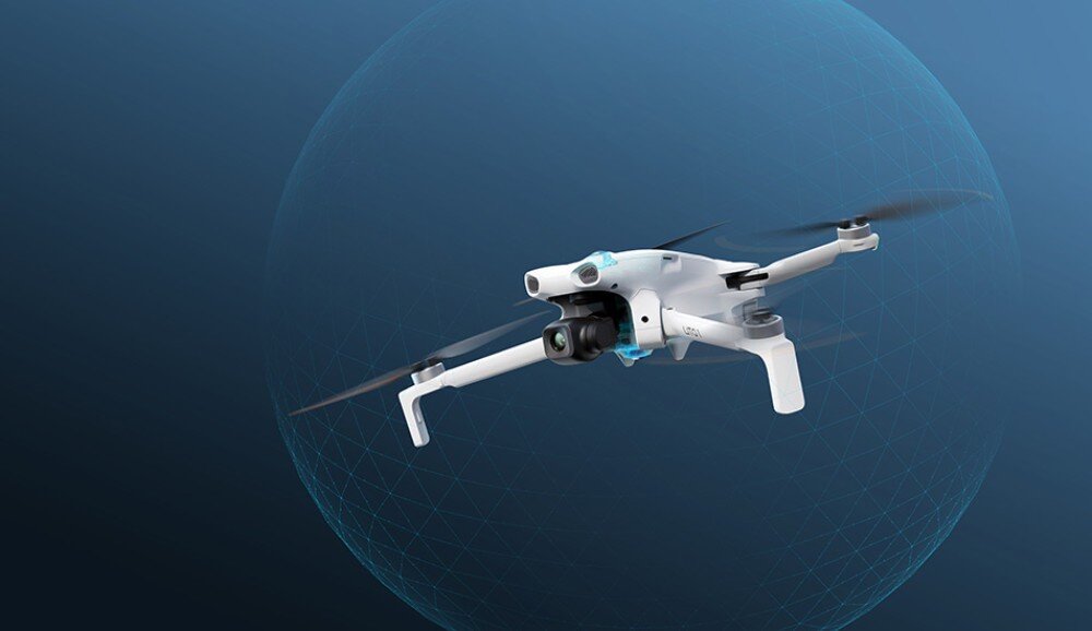 Na obrazie widoczny jest biały dron z czterema śmigłami, unoszący się w powietrzu na tle niebieskiego gradientu z delikatnym wzorem siatki. Dron ma zamontowaną kamerę i kilka czujników.