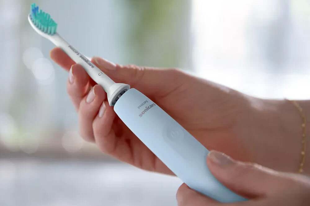Osoba trzyma niebieską szczoteczkę soniczną z widocznym napisem \'PHILIPS Sonicare\'.