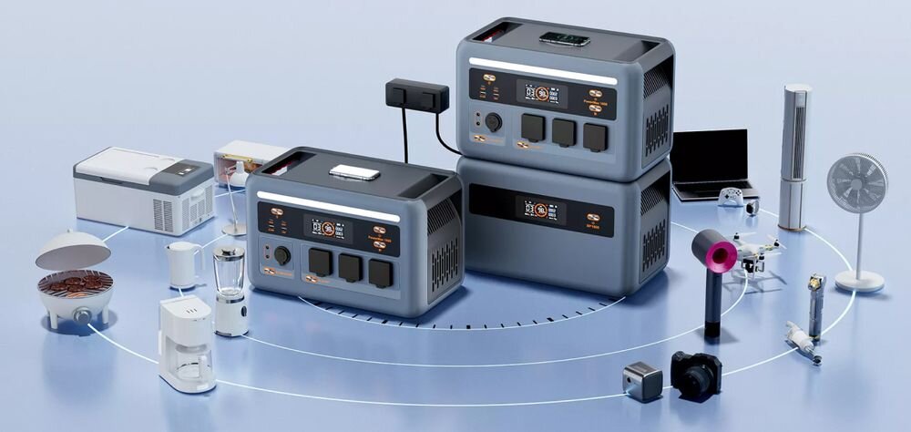 Na obrazie widoczne są dwie szare stacje zasilania z wyświetlaczami i gniazdami, otoczone różnymi urządzeniami elektronicznymi na niebieskim tle. W tle znajdują się m.in. wentylator, suszarka do włosów i kamera.
