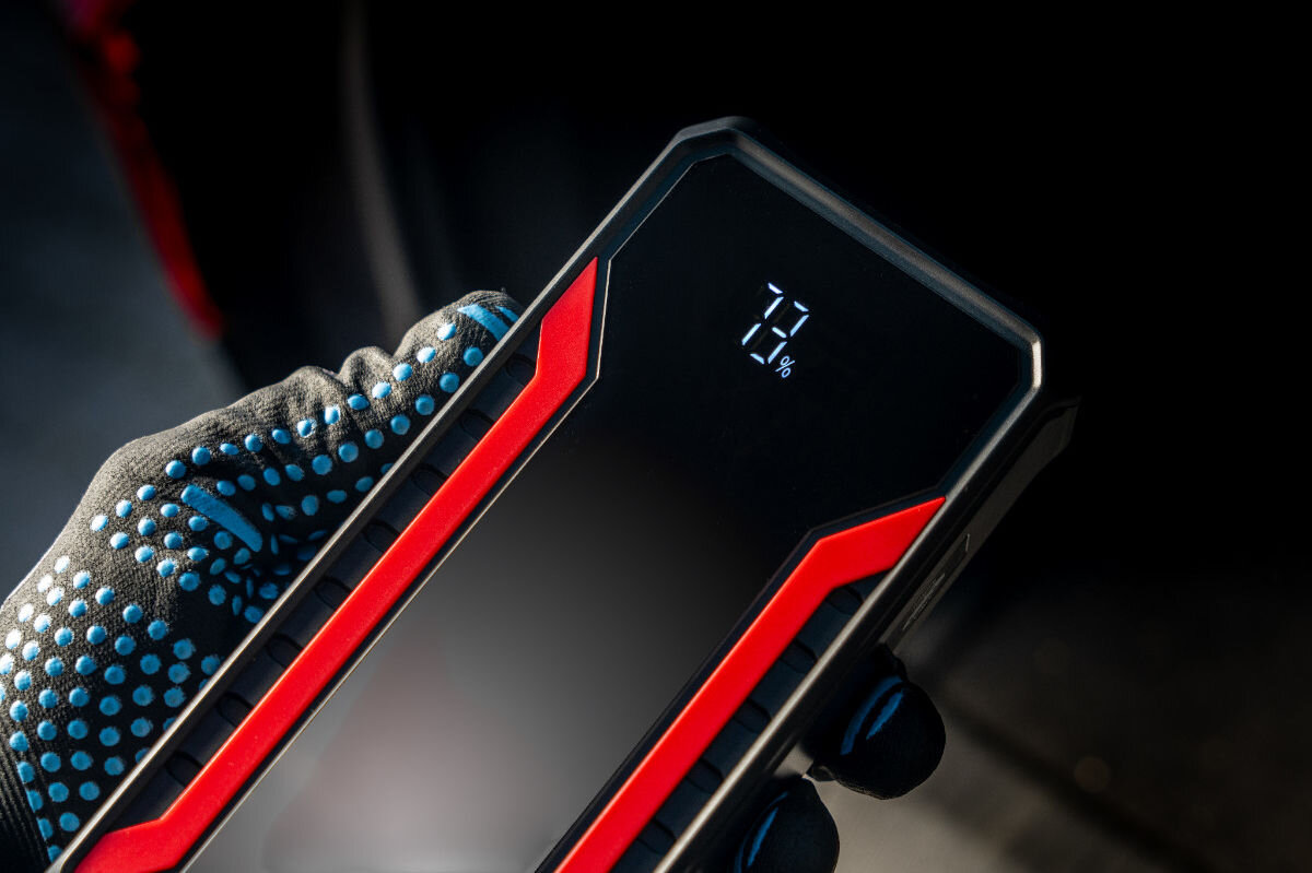 Osoba w rękawicy trzyma czarny powerbank z czerwonymi akcentami, na którym wyświetla się napis \'73%\'.