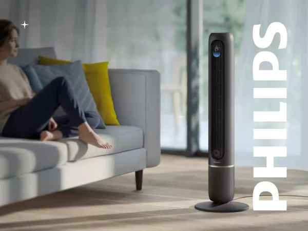 Ciemnoszary wentylator stojący w nowoczesnym wnętrzu, obok kanapy z poduszkami. Na obrazie widoczne jest logo \'PHILIPS\'.