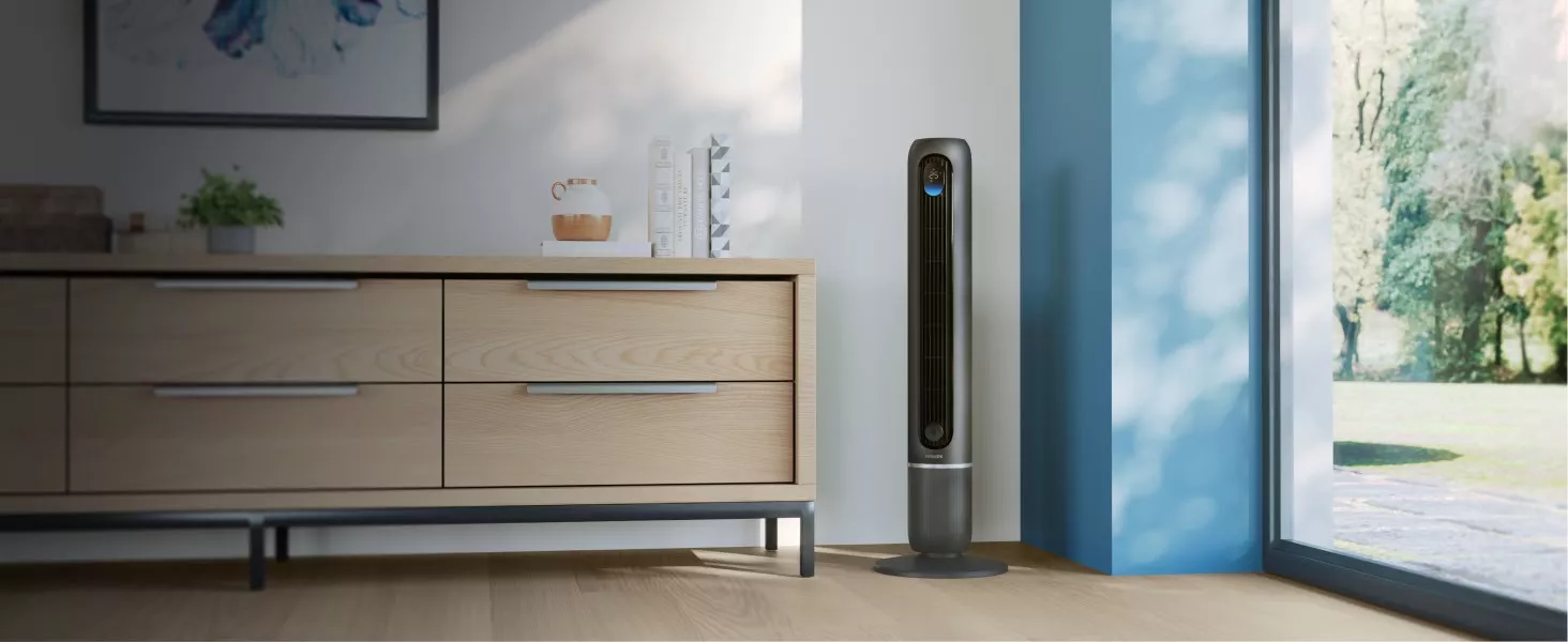 W jasnym pomieszczeniu stoi ciemnoszary wentylator kolumnowy z widocznym logo PHILIPS. Obok znajduje się drewniana komoda z kilkoma przedmiotami na blacie.