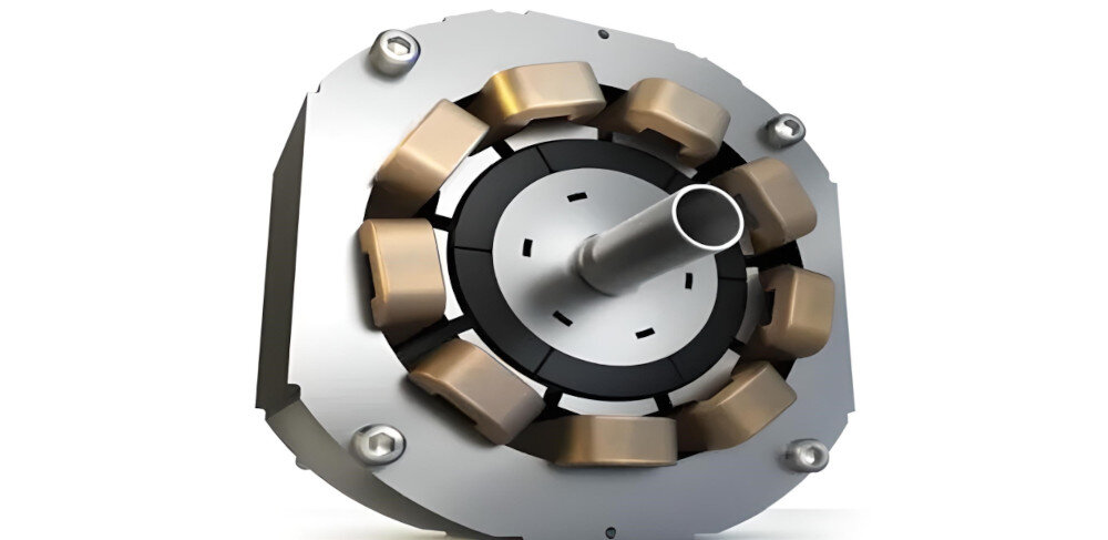 Obraz przedstawia metalowy element mechaniczny z centralnym wałkiem i kilkoma miedzianymi cewkami rozmieszczonymi wokół niego. Element jest zamocowany na okrągłej podstawie z czterema śrubami.