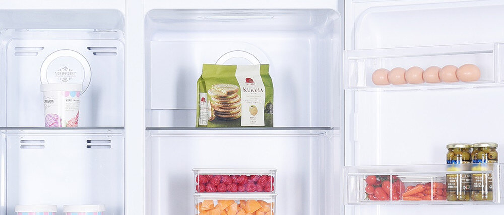 Wnętrze lodówki z widocznymi półkami, na których znajdują się różne produkty spożywcze, takie jak jajka, owoce, warzywa, opakowania z żywnością oraz słoiki z przetworami. Na jednej z półek widoczny jest napis \'NO FROST\'.