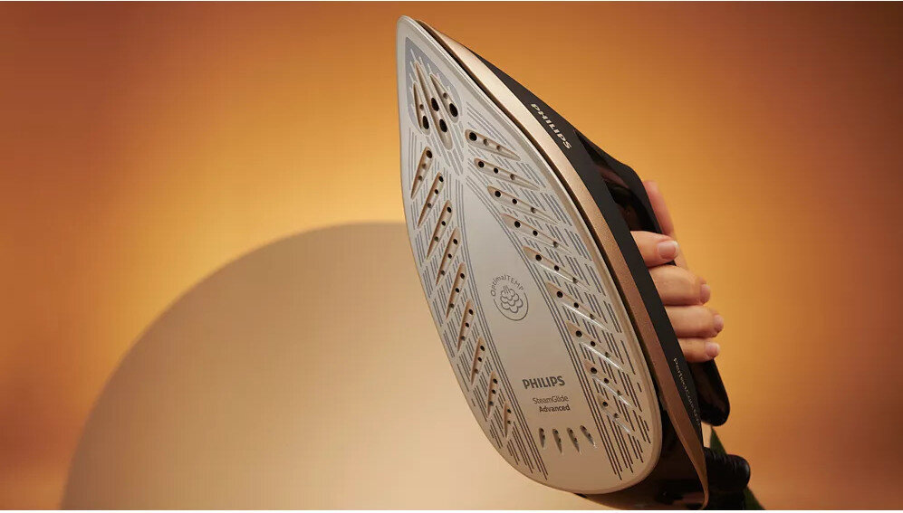 Zdjęcie przedstawia stopę żelazka z widocznymi otworami parowymi i napisem \'PHILIPS SteamGlide Advanced\'. W tle znajduje się rozmyte, pomarańczowe tło.