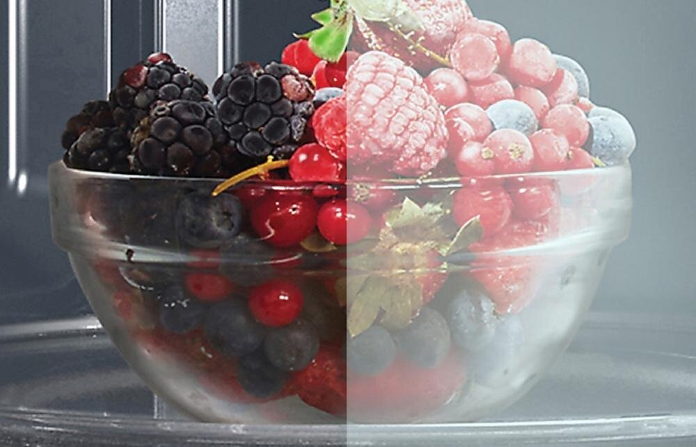 Szklana miska wypełniona różnymi owocami jagodowymi, takimi jak maliny, jeżyny i borówki, umieszczona wewnątrz kuchenki mikrofalowej. Obraz jest podzielony na dwie części, z różnicą w oświetleniu lub kolorystyce.