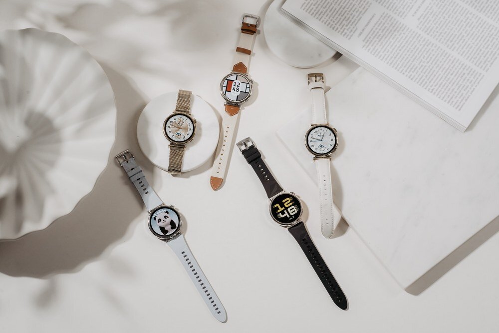 Na obrazie znajduje się pięć smartwatchy z różnymi tarczami i paskami, ułożonych na jasnym tle. Każdy zegarek ma inny wzór tarczy, w tym cyfry, wzory geometryczne i grafikę pandy.