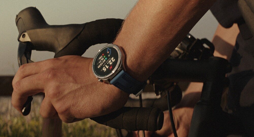 Osoba trzyma kierownicę roweru, na nadgarstku ma smartwatch z kolorowym wyświetlaczem pokazującym godzinę 22:15.