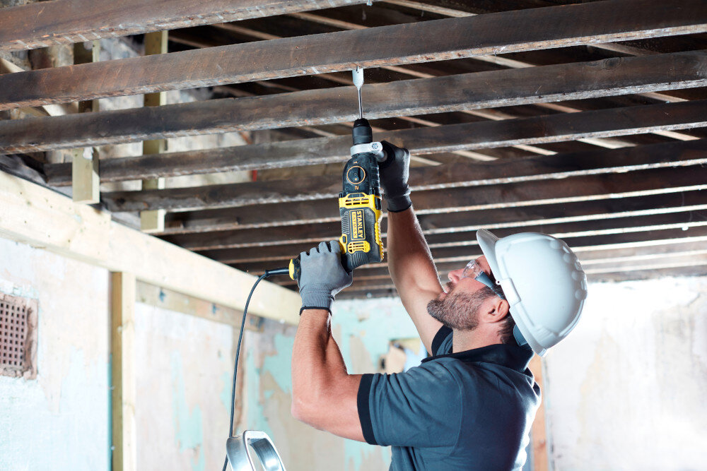 Wiertarka udarowa STANLEY FMEH1100K plac budowy osoba wierci otwór w drewnianym elemencie sufitu moc wydajność precyzja wszechstronność