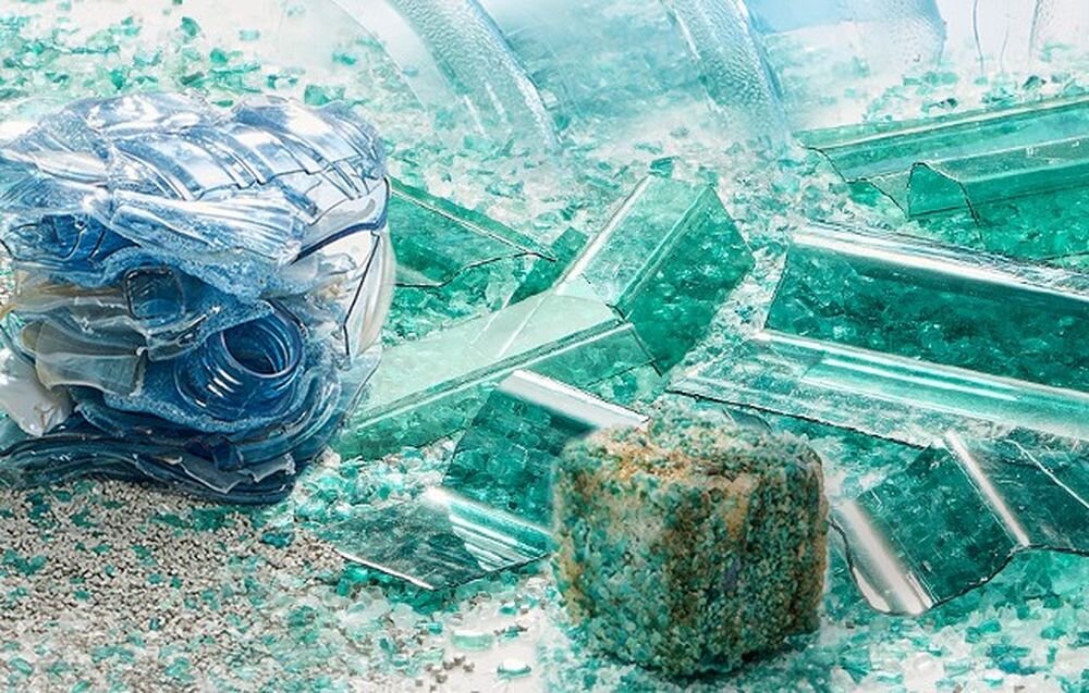 Obraz przedstawia stos pokruszonego szkła i plastikowych elementów w odcieniach zieleni i niebieskiego. W tle widoczne są większe kawałki szkła oraz bryła przypominająca kamień.