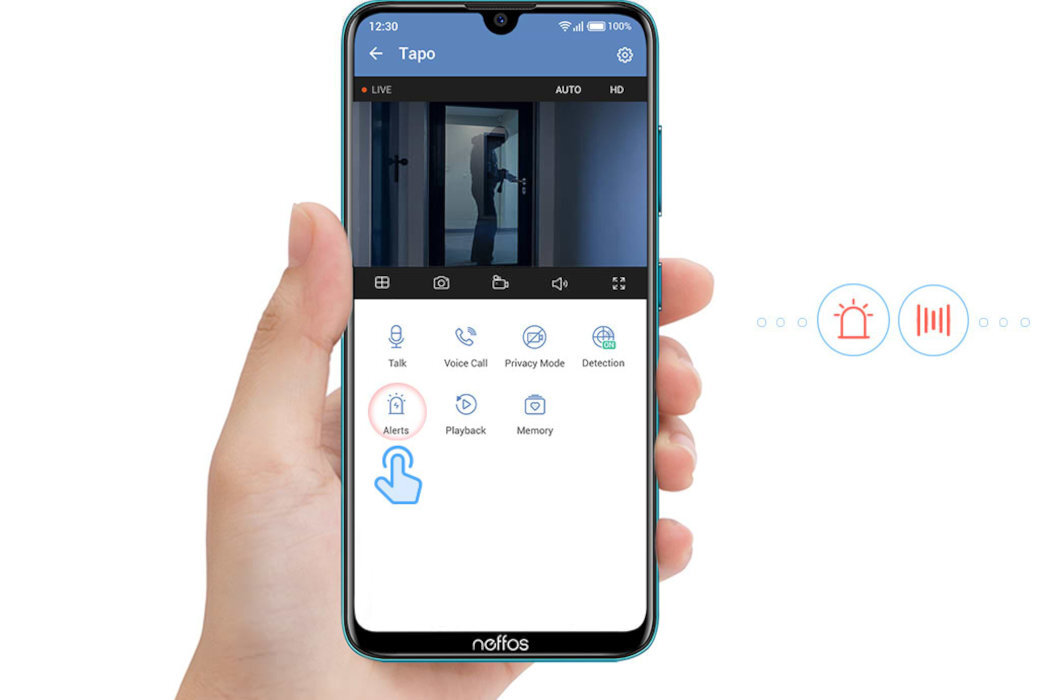 Osoba trzyma smartfon z aplikacją Tapo, na ekranie widoczny jest podgląd z kamery oraz ikony: Talk, Voice Call, Privacy Mode, Detection, Alerts, Playback, Memory. W tle widać ikonę alarmu i wykresu dźwięku.