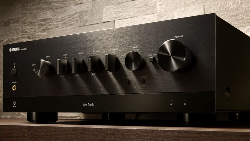 Czarny amplituner stereo z kilkoma pokrętłami i przyciskami na przednim panelu. Widoczne logo \'YAMAHA\' oraz napis \'Net Radio\'.