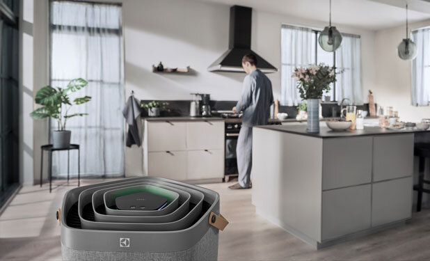 W nowoczesnej kuchni znajduje się oczyszczacz powietrza z widocznym logo Electrolux. W tle osoba przygotowuje posiłek przy kuchence.