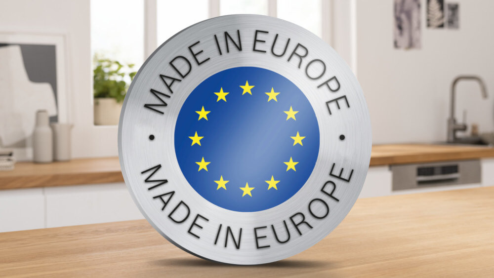 Okrągły emblemat z napisem \'MADE IN EUROPE\' otacza niebieskie koło z dwunastoma żółtymi gwiazdami. W tle widoczna jest kuchnia z drewnianym blatem i zlewem.