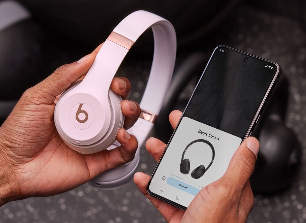 Osoba trzyma różowe słuchawki nauszne z logo \'b\' oraz smartfon z wyświetlonym obrazem słuchawek i napisem \'Beats Solo 4\'.