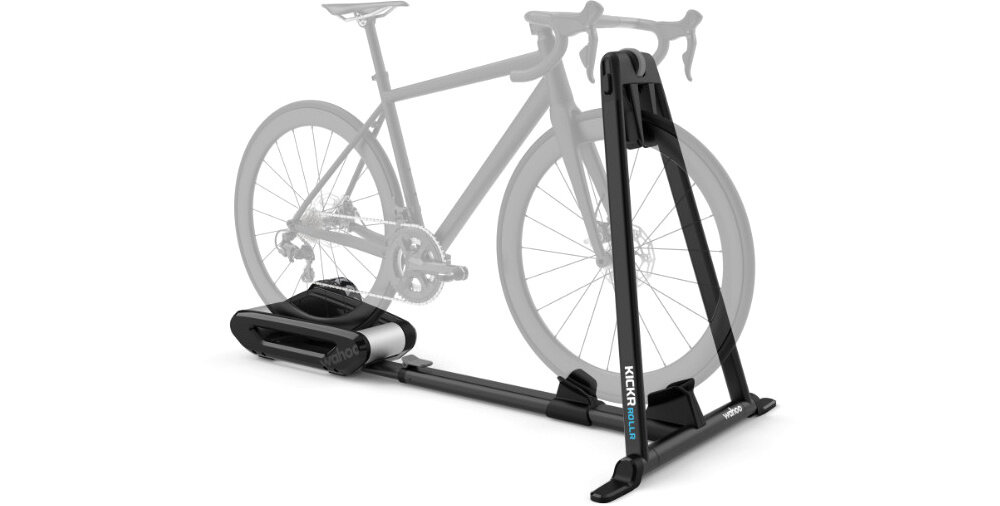 Na obrazie widoczny jest trenażer rowerowy z czarną ramą i miejscem na tylne koło roweru. Na ramie znajduje się napis \'KICKR ROLLR\'.
