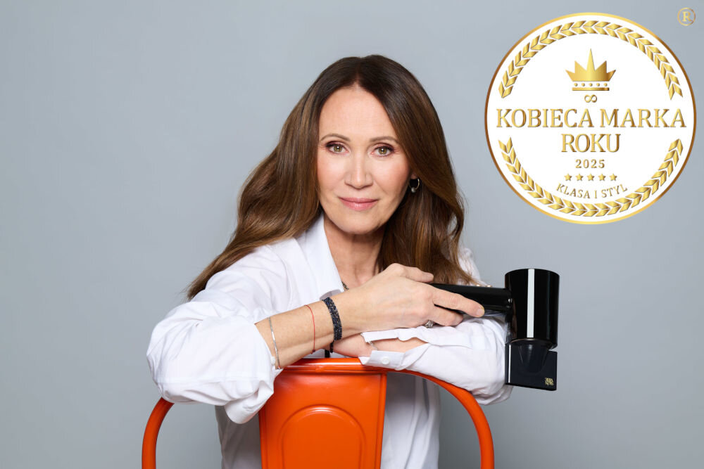 Osoba w białej koszuli trzyma czarną suszarkę do włosów, opierając się o pomarańczowy element. Obok znajduje się złoty emblemat z napisem \'KOBIECA MARKA ROKU 2025 KLASA I STYL\'.