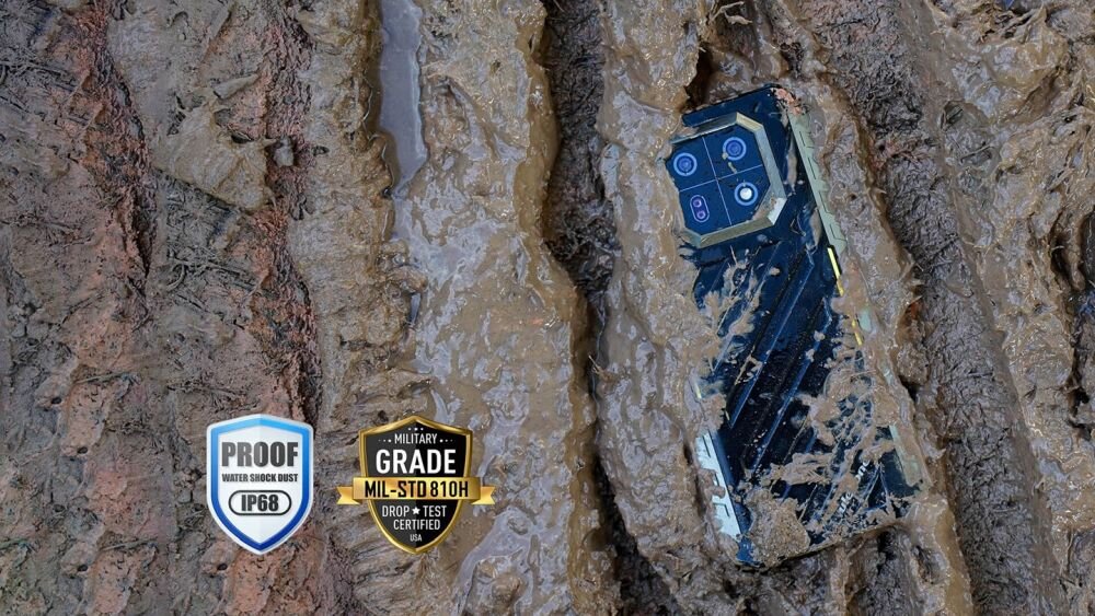 Smartfon częściowo zanurzony w błocie, widoczne są cztery obiektywy aparatu. Obok znajdują się dwa emblematy: \'PROOF WATER SHOCK DUST IP68\' oraz \'MILITARY GRADE MIL-STD 810H DROP TEST CERTIFIED\'.