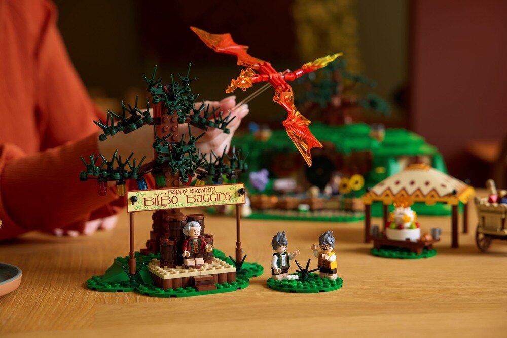 Zestaw LEGO przedstawiający scenę z postaciami i elementami krajobrazu, w tym drzewem i namiotem. Na tabliczce widnieje napis \'Happy Birthday Bilbo Baggins\'.