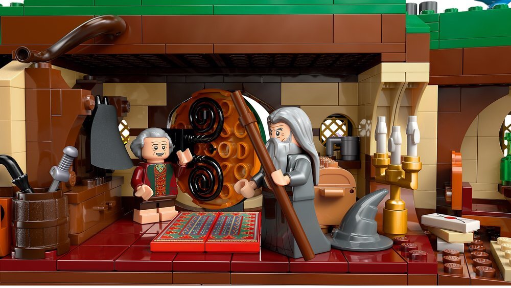 Zestaw LEGO przedstawiający wnętrze domu z okrągłymi drzwiami, dwoma figurkami postaci, świecznikiem i różnymi akcesoriami. W tle widoczne są okna z kratkami i zielony dach.